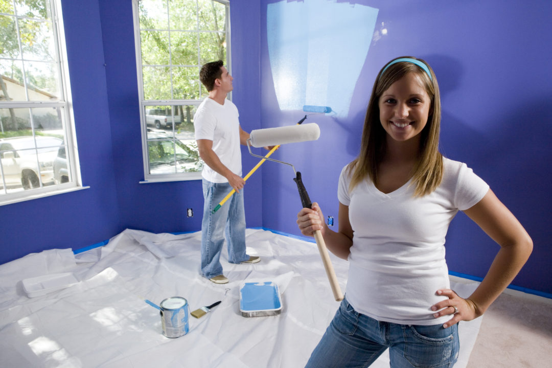 Portrait of a cheerful young woman holding paint roller while young man painting wall
