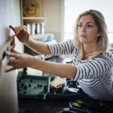 Mature woman using a spirit level and marking the wall with a pencil in her kitchen.
