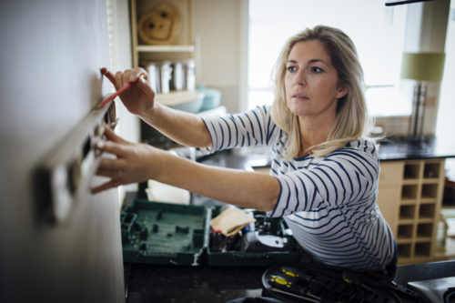 Mature woman using a spirit level and marking the wall with a pencil in her kitchen.