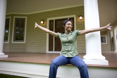 New home owner sitting on porch of suburban home with arms outstretched, showing it off